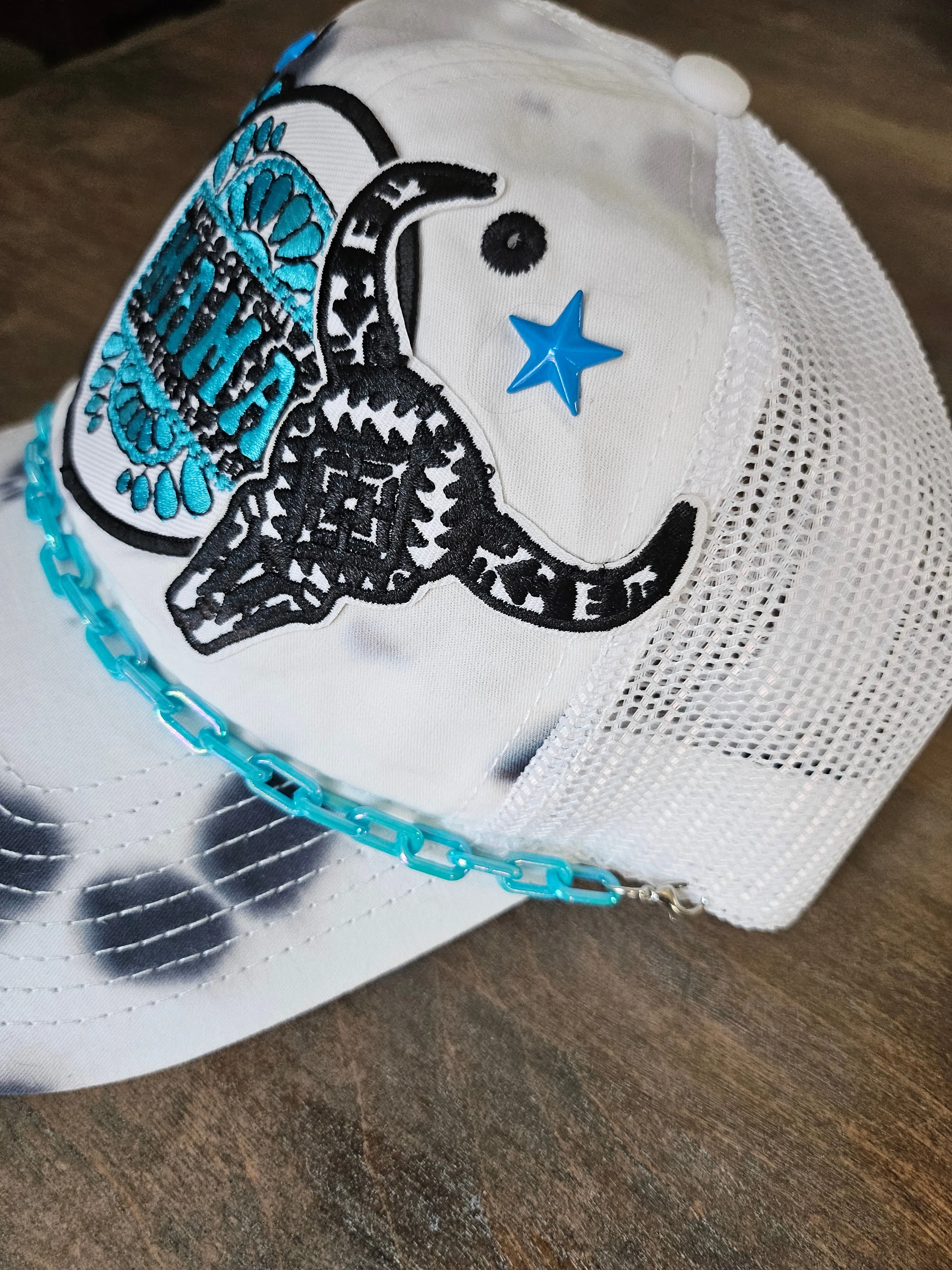 Tie dye trucker hat in black and turquoise with "mama", bullhead, and roses patches.