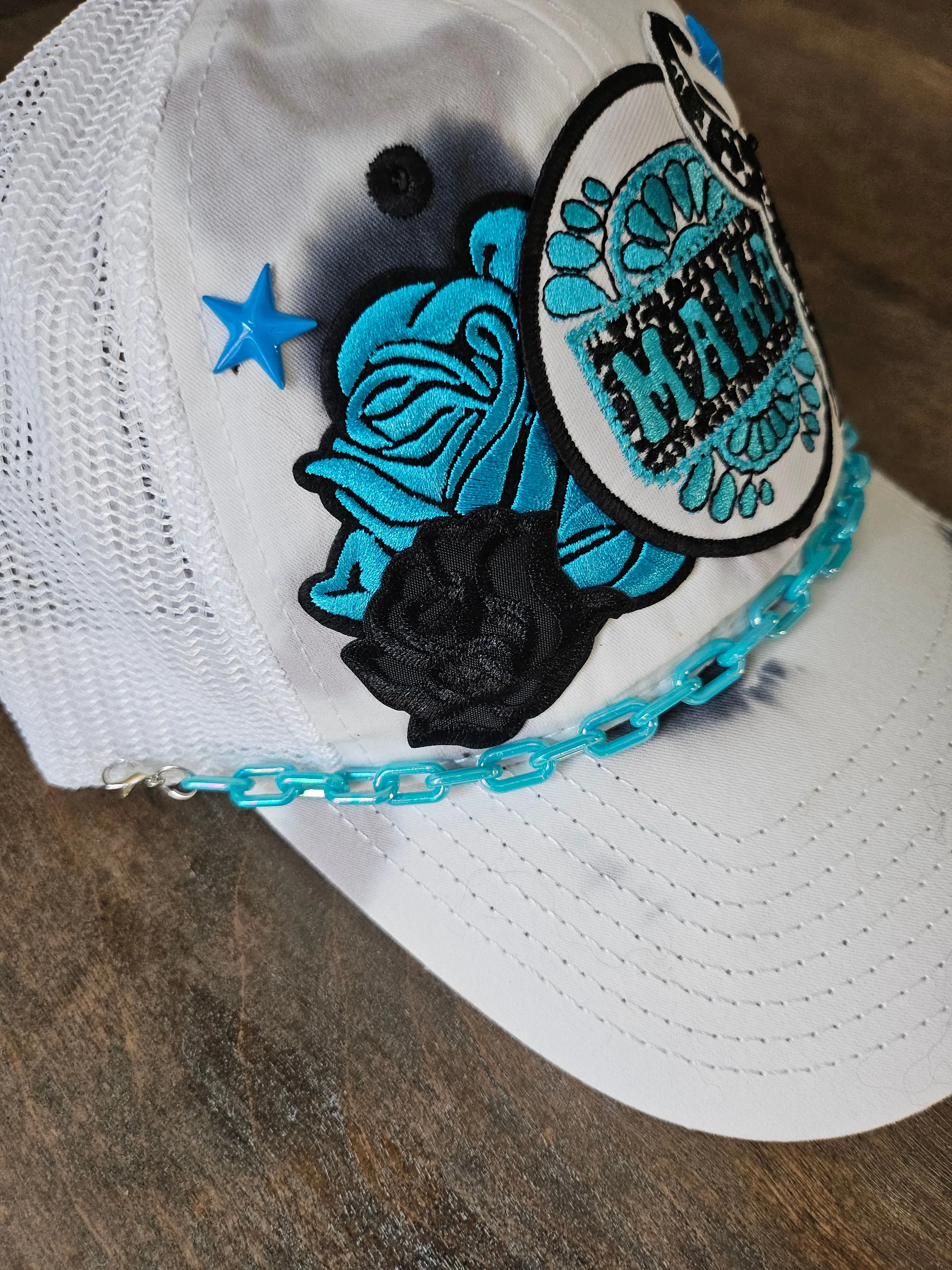 Tie dye trucker hat in black and turquoise with "mama", bullhead, and roses patches.